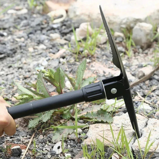 The folding shovel set as a pick, its point driven into gravelly ground